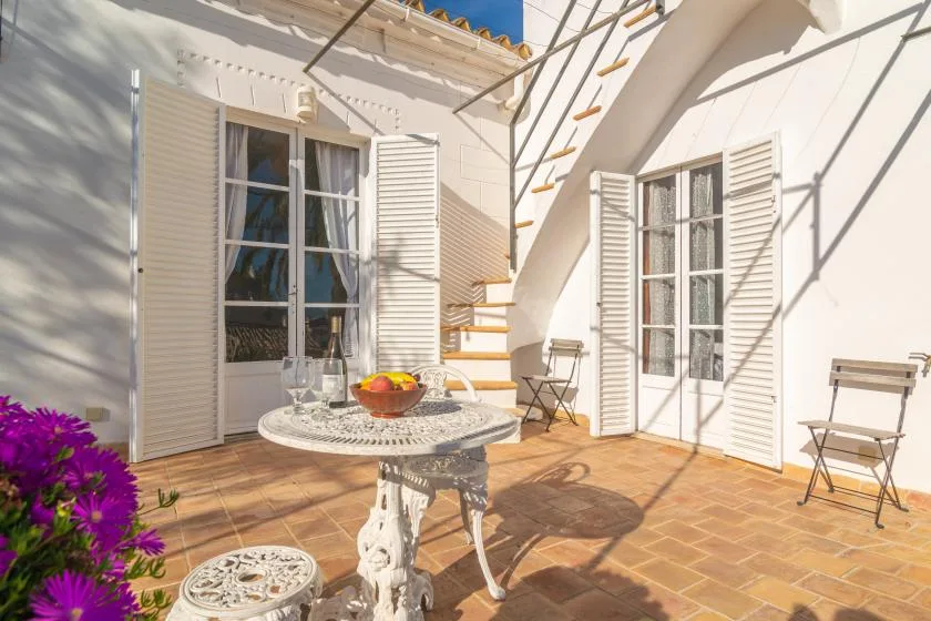 A sunny patio with a round table, shuttered windows, and an exterior staircase.