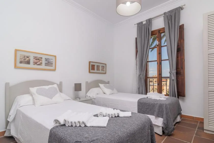 A bright bedroom with two beds, gray curtains, and framed pictures on the walls.