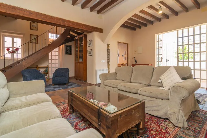 A living room with beige seating, a glass-topped coffee table, and exposed ceiling beams.