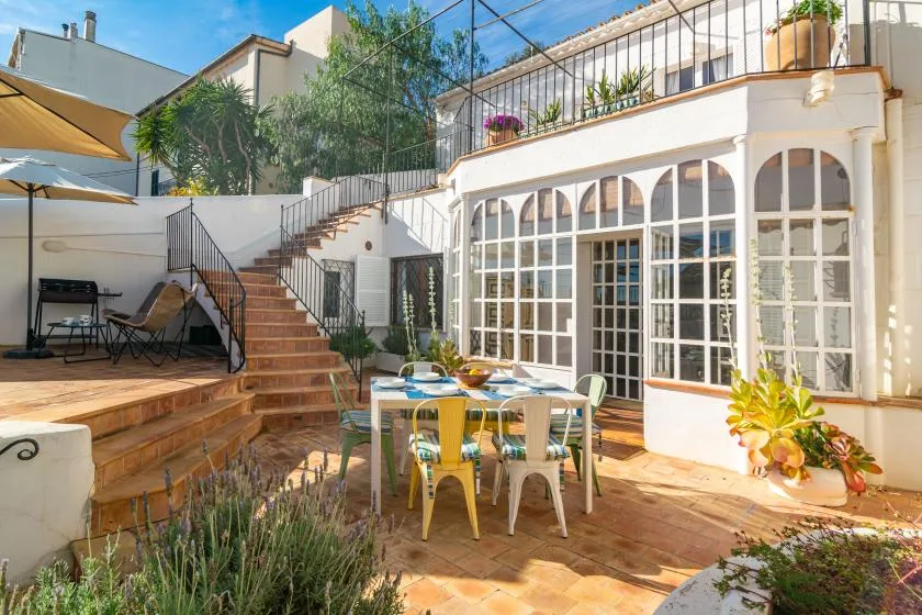 Un patio soleado con una mesa de comedor, asientos al aire libre y escaleras hacia una terraza superior.