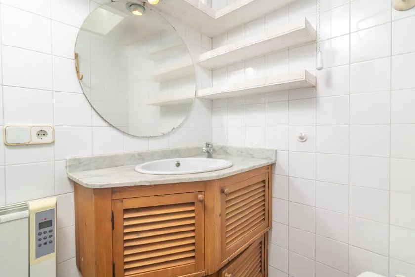 A tiled bathroom with a wooden vanity, sink, and round mirror.