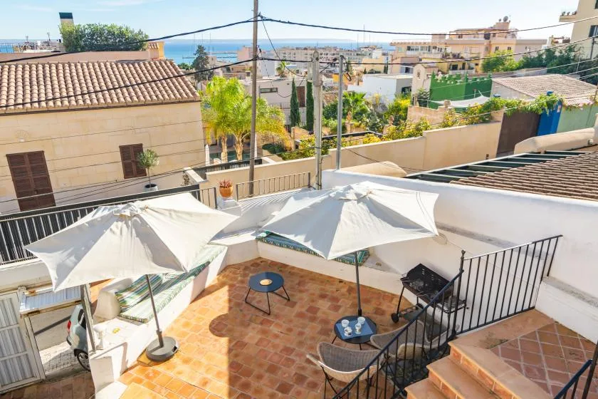 Una terraza en la azotea con asientos a la sombra y vistas a edificios cercanos y al mar.