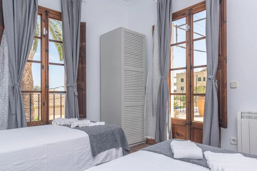 A bright bedroom with two beds and tall windows framed by gray curtains.