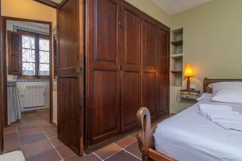 A bedroom with a bed beside a large wooden wardrobe and an open doorway.