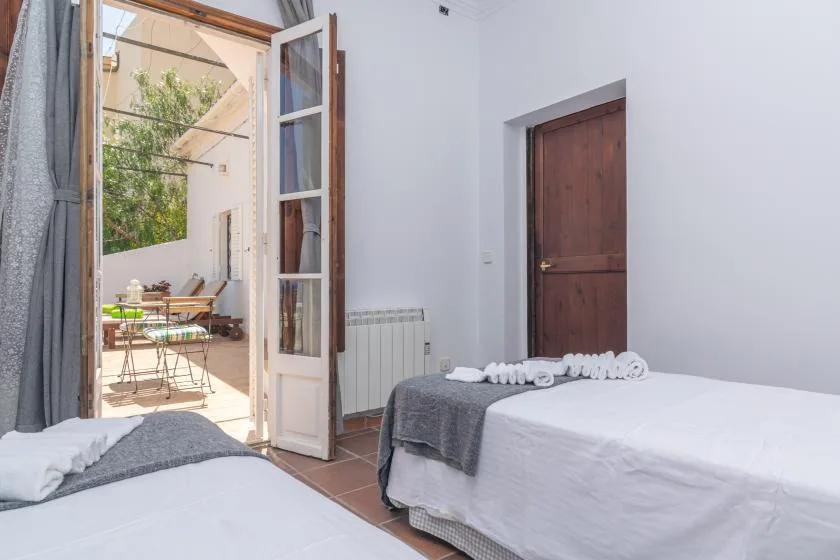 A bedroom with beds beside an open glass door leading to a terrace.