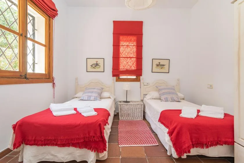 A bedroom with two beds dressed in red and white bedding.