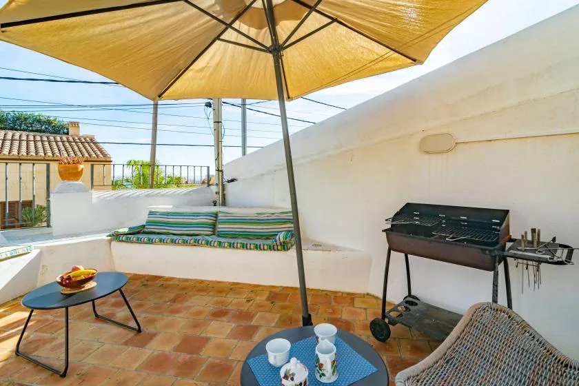 A tiled outdoor terrace has a large umbrella, seating, and a barbecue grill.