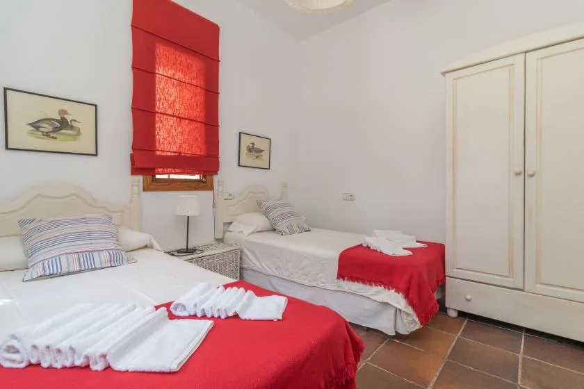 A bedroom with two beds, red bedding, and a wardrobe.