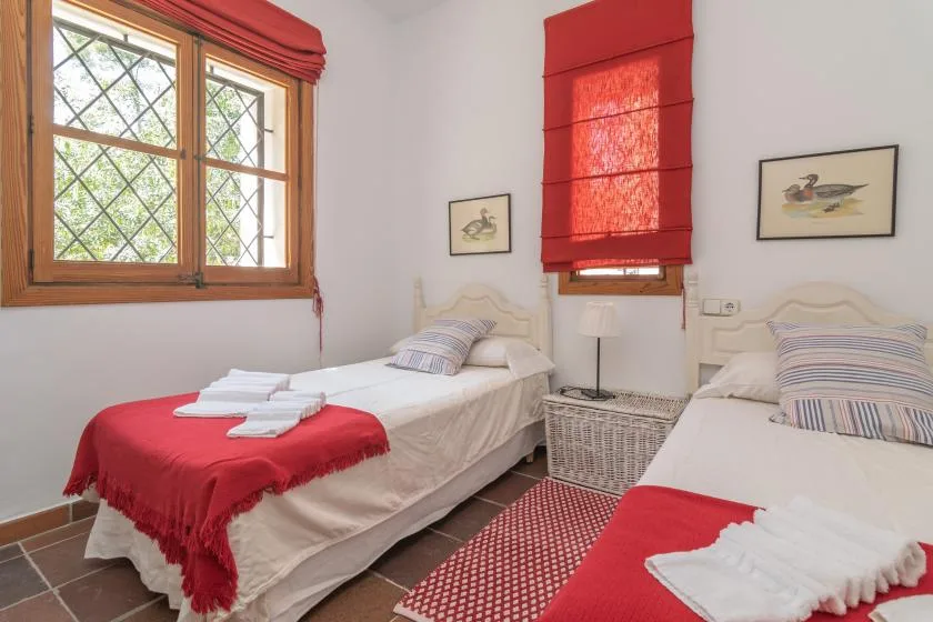 A bedroom with two beds, red window shades, and folded towels on the bedding.