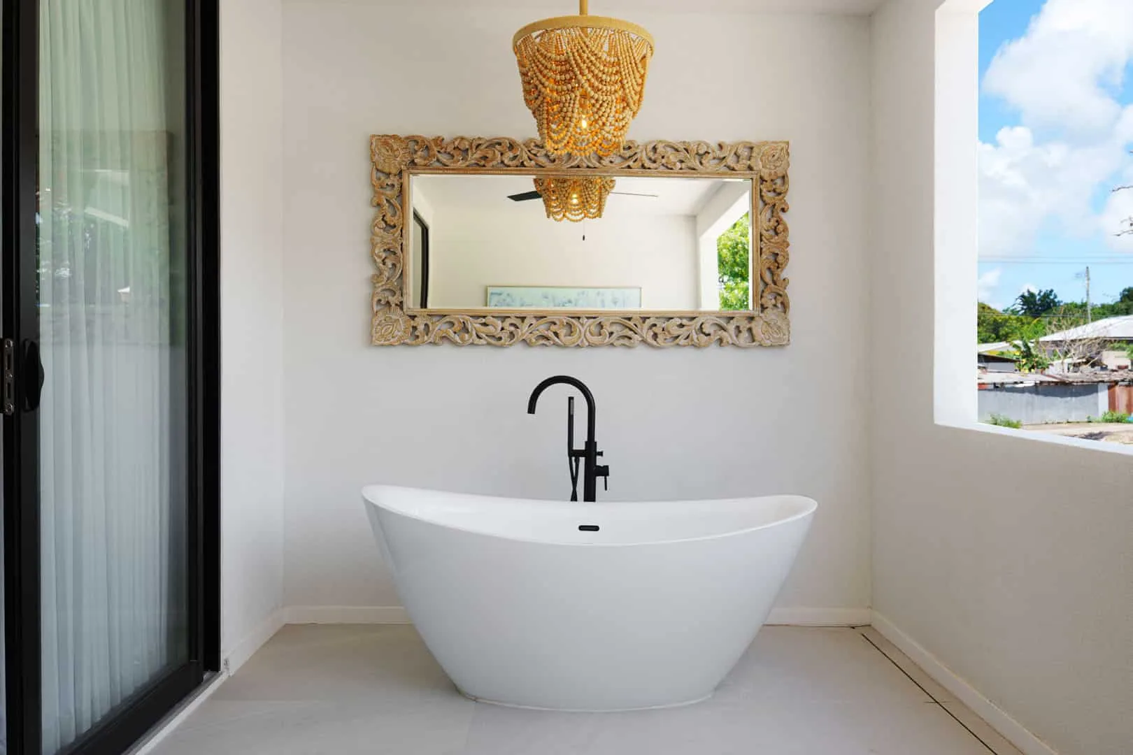 Una bañera exenta está debajo de un espejo decorativo en un baño luminoso.