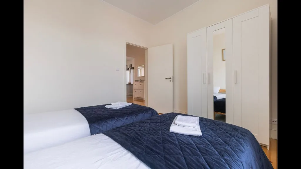 Un dormitorio con dos camas vestidas con sábanas blancas y colchas azul oscuro.