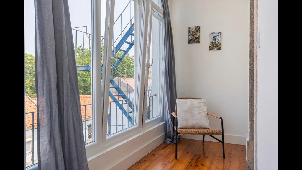 Una habitación luminosa con una silla junto a grandes ventanas y cortinas grises.