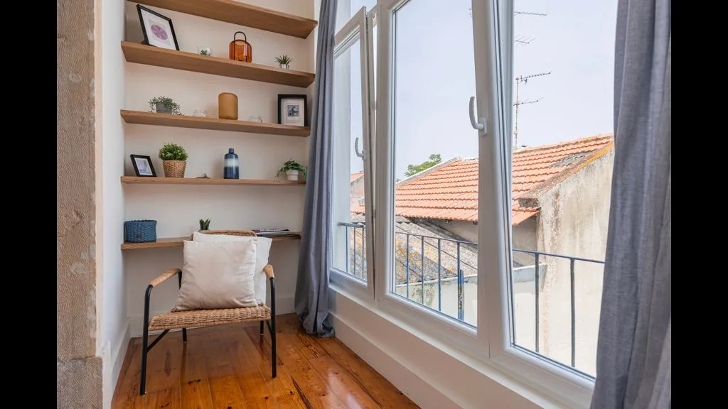 Una habitación luminosa con un asiento acolchado junto a grandes ventanas con vistas a tejados.