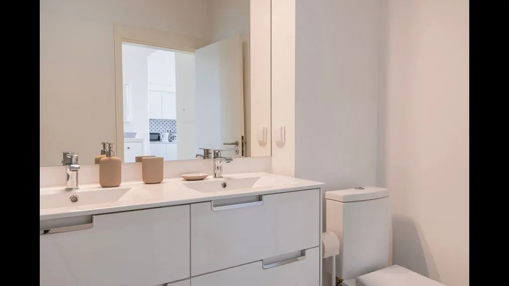 Un baño luminoso con un tocador de dos lavabos y un inodoro.
