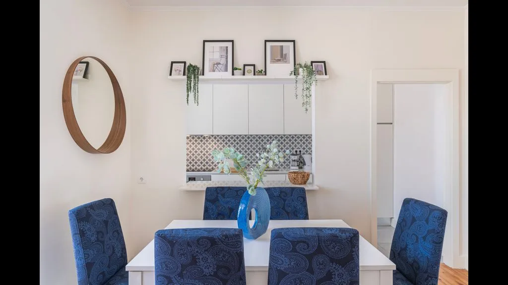 Un comedor luminoso con asientos azules alrededor de una mesa blanca y cuadros enmarcados.