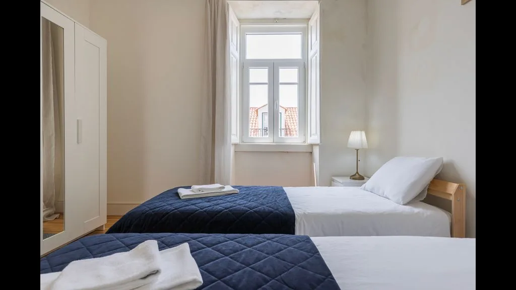 Un dormitorio con dos camas, arregladas con sábanas blancas y mantas azules.