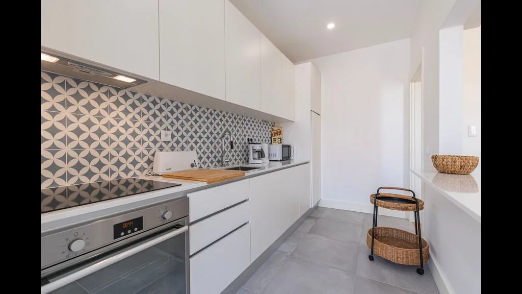 Una cocina moderna con gabinetes blancos, un salpicadero estampado y un horno integrado.