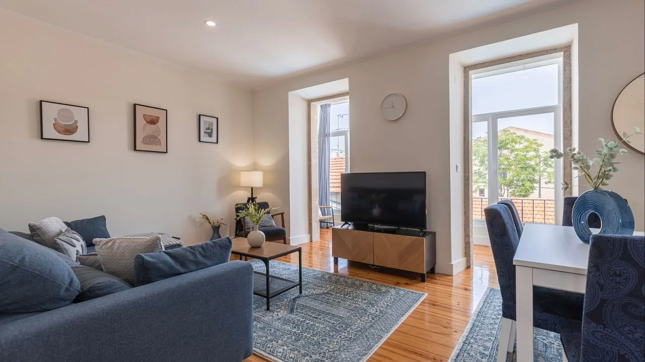 Una sala de estar con asientos, un televisor y una mesa de comedor junto a las ventanas.