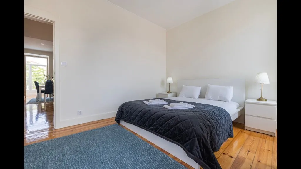Un dormitorio con una cama cubierta con una colcha oscura y una alfombra azul.