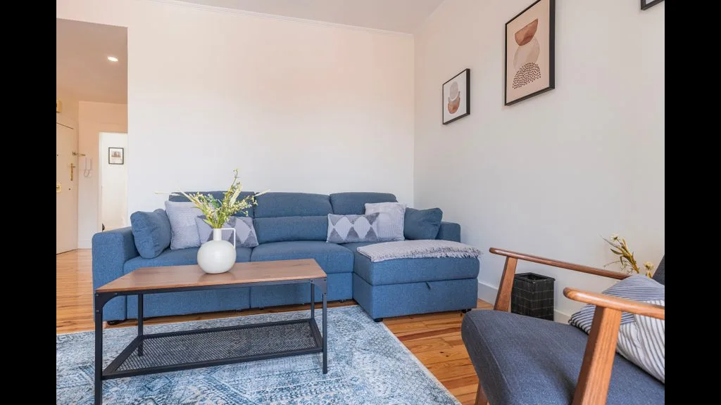 Una sala de estar con asientos azules, una mesa de centro de madera y cuadros en la pared.