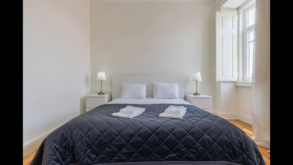 Un dormitorio con una cama cubierta por una colcha oscura y una ventana.