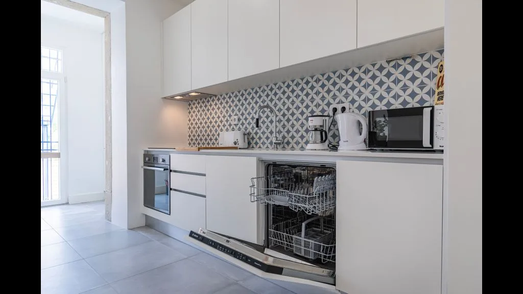 Una cocina moderna con gabinetes blancos, salpicadero estampado y un lavavajillas abierto.
