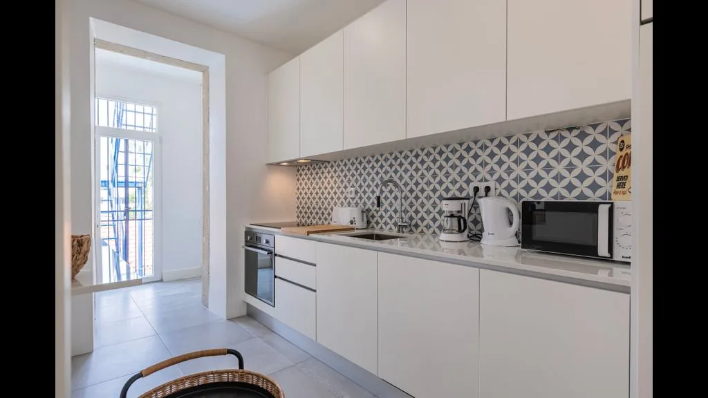 Una cocina moderna con gabinetes blancos, salpicadero estampado y electrodomésticos sobre la encimera.