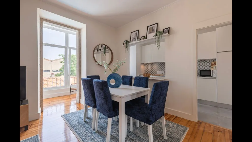 Comedor con una mesa y asientos tapizados en azul junto a una ventana luminosa.