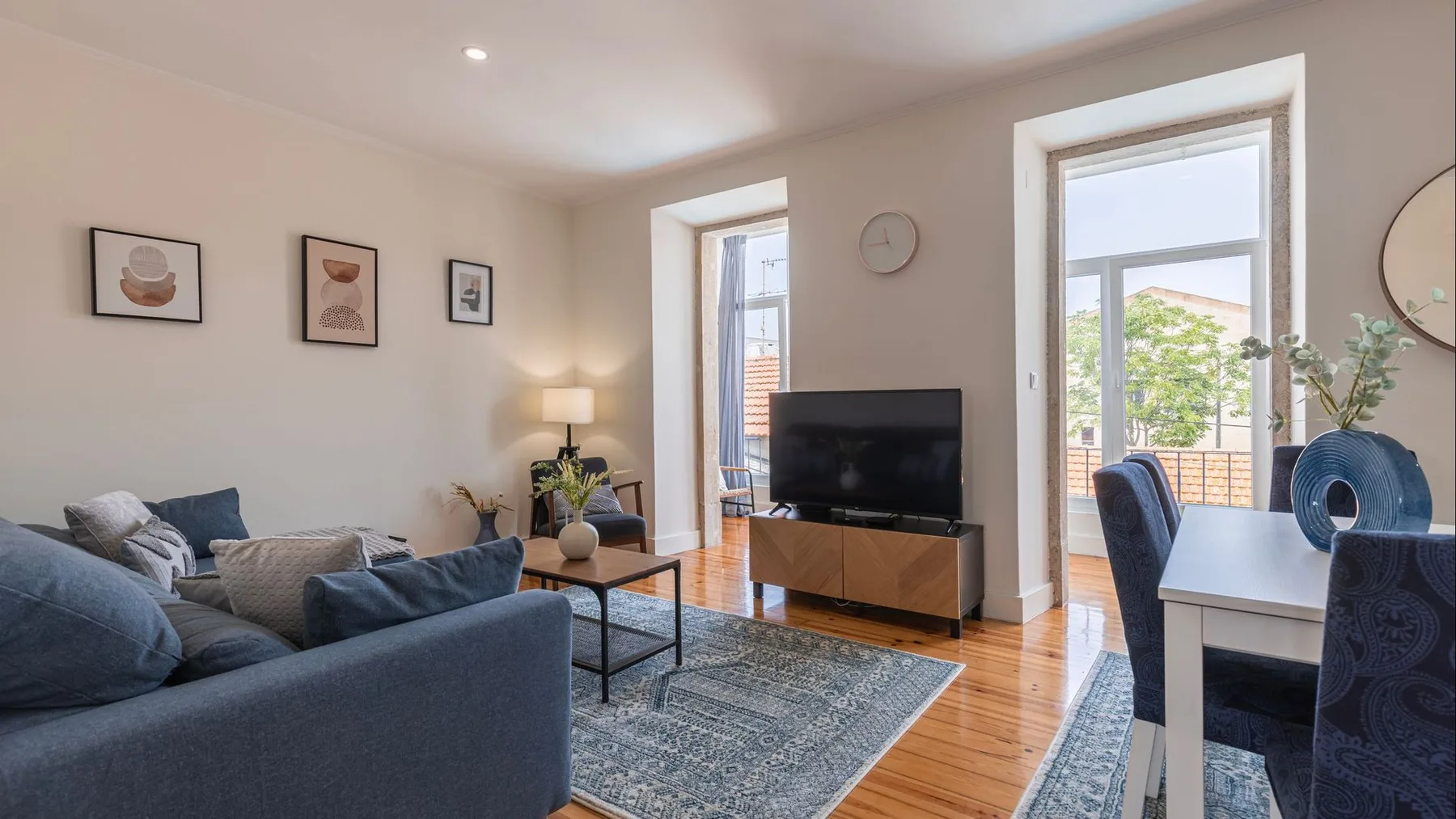 Una sala luminosa con asientos, un televisor y un comedor junto a las ventanas.