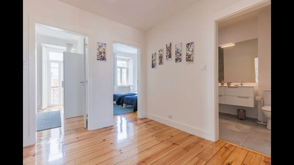 Una habitación luminosa con suelo de madera da a un dormitorio y un baño.