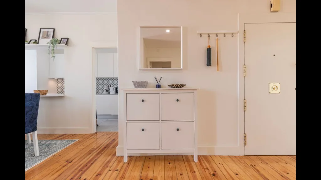 Un recibidor luminoso con un mueble blanco, un espejo de pared y suelo de madera.