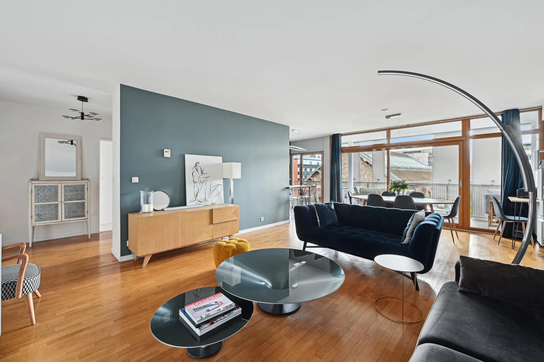 A modern living room with seating, a glass coffee table, and large windows.