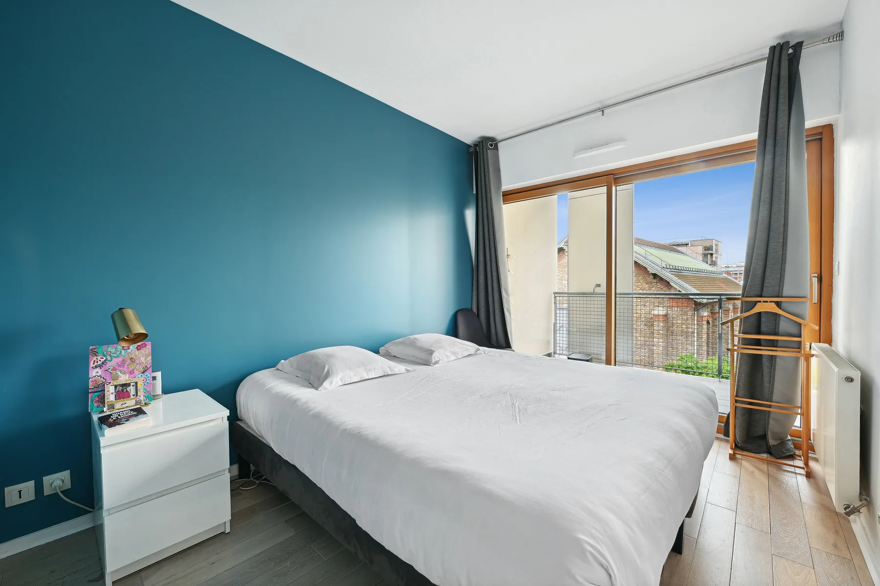 A bedroom with a large bed beside full-height windows and gray curtains.