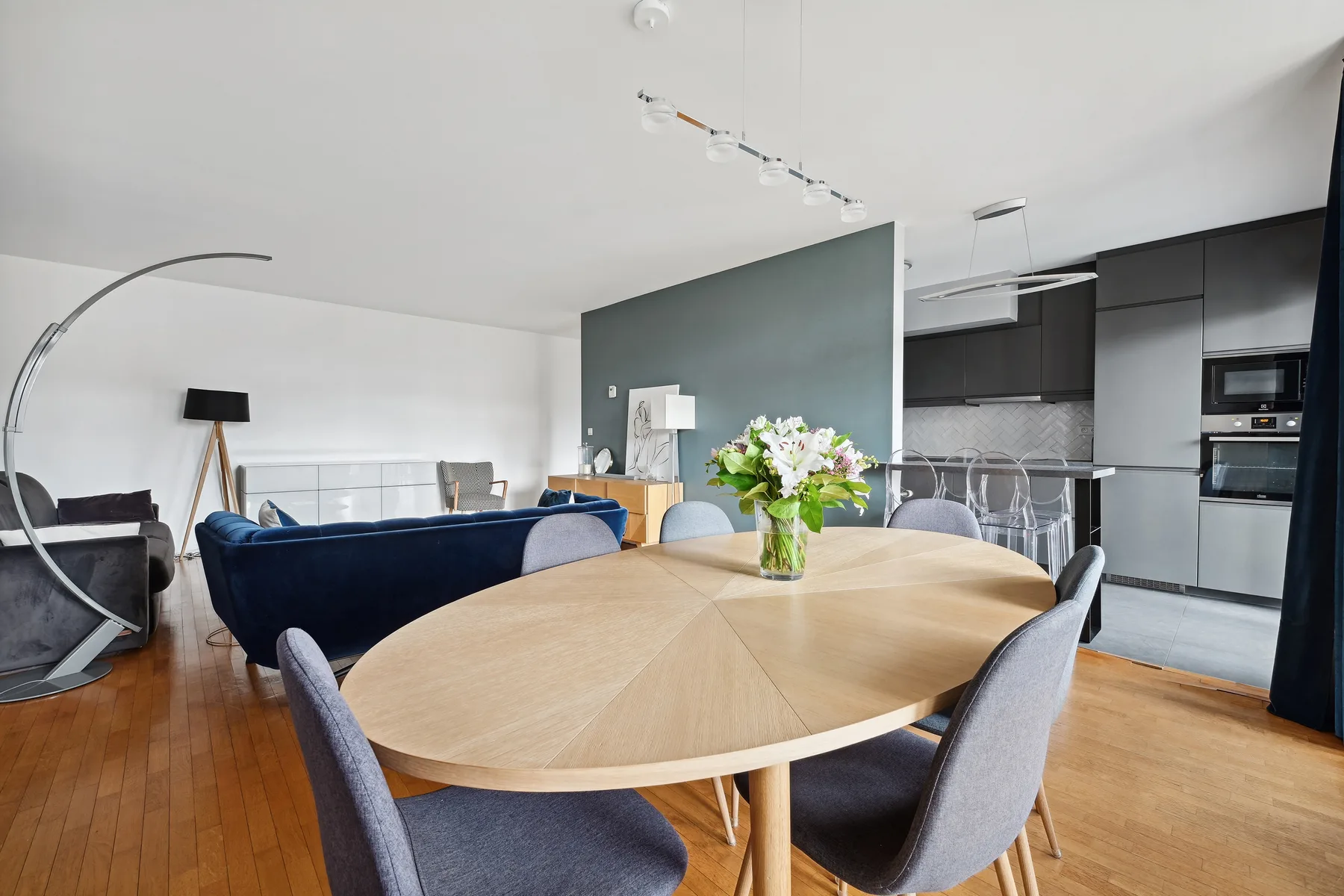 A dining area with a round wooden table and an open kitchen beyond.
