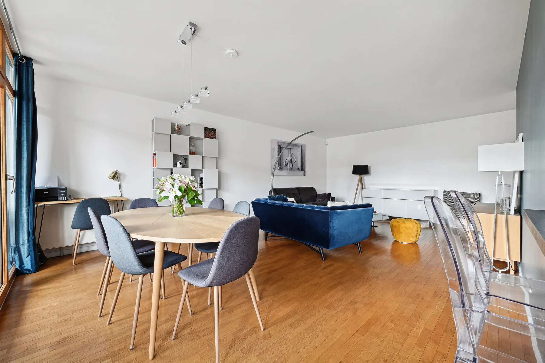 A bright open-plan living and dining room with a blue sofa and wooden table.