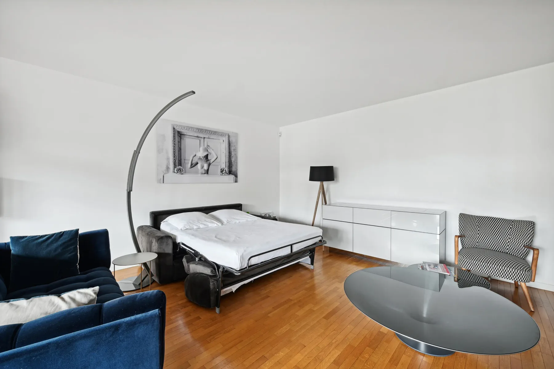 A modern bedroom with a bed, blue seating, and a glass coffee table.