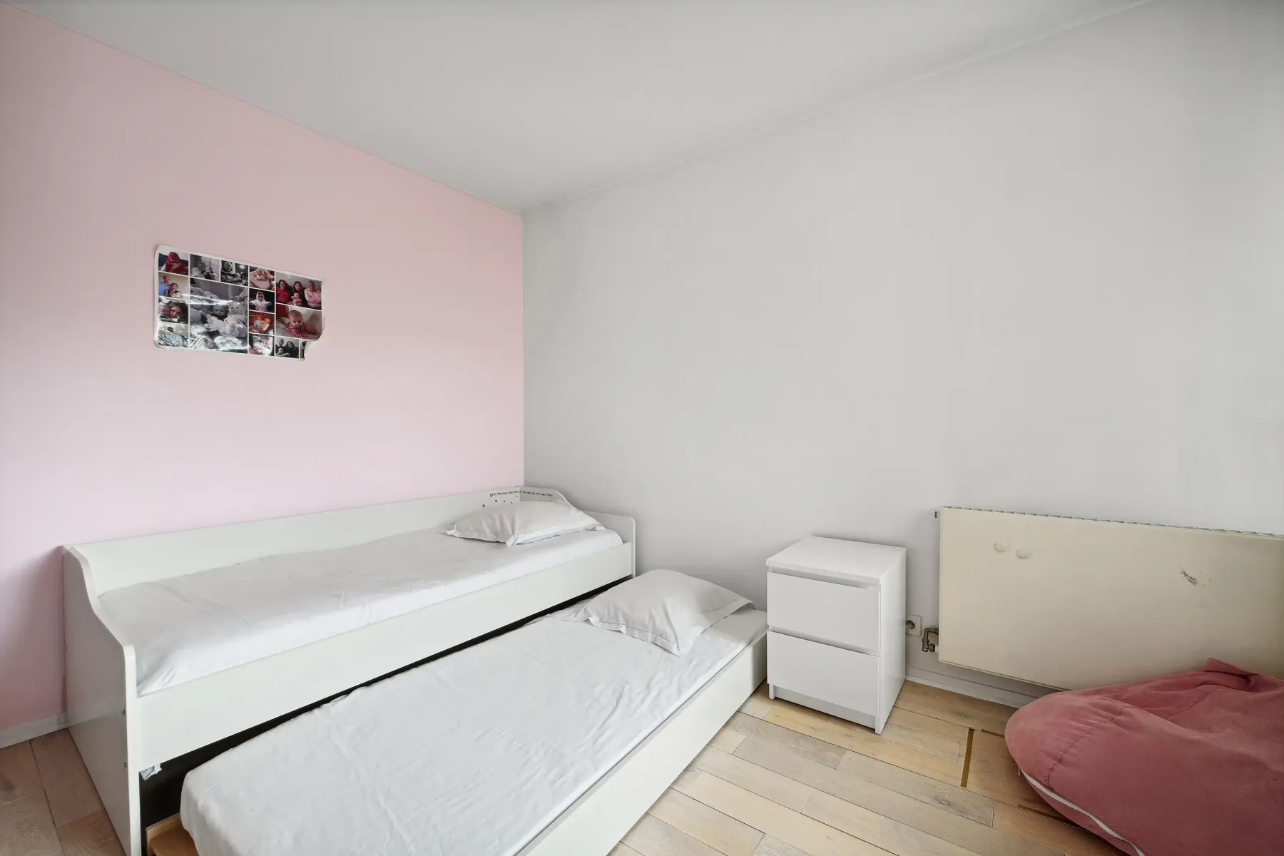 A bedroom with two low beds, a small drawer unit, and a pink wall.