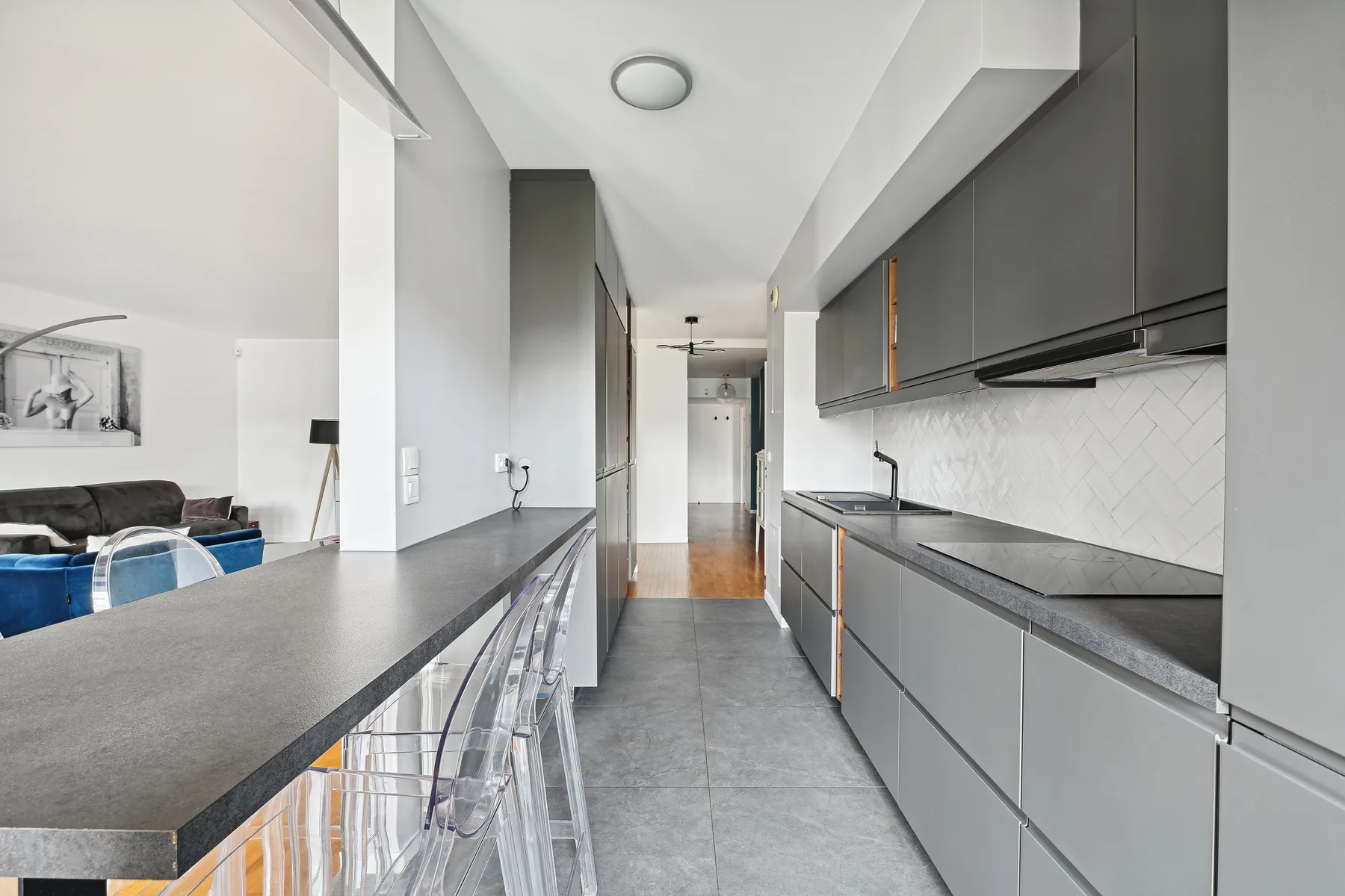A modern kitchen with gray cabinets, a long counter, and clear stools.
