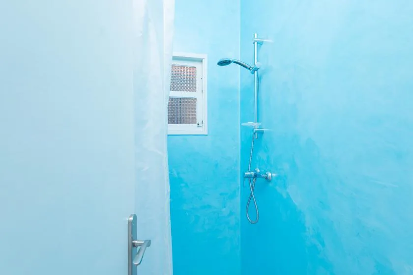 A bathroom shower area with bright blue walls and a small window.