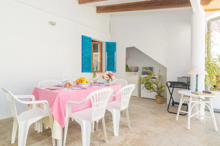 A bright covered patio with a pink-covered dining table and white seating.