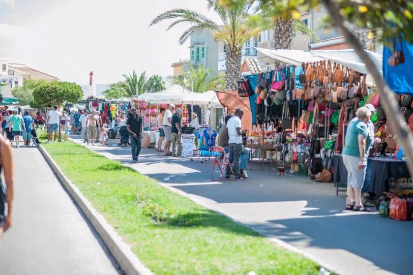 An outdoor market with clothing stalls lining a sunny pedestrian walkway.