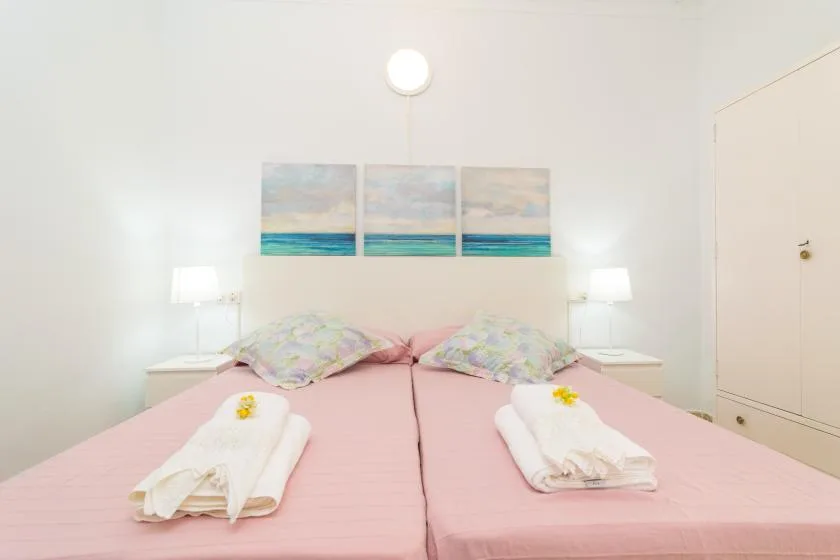A bright bedroom with two beds dressed in pink and beach artwork above them.