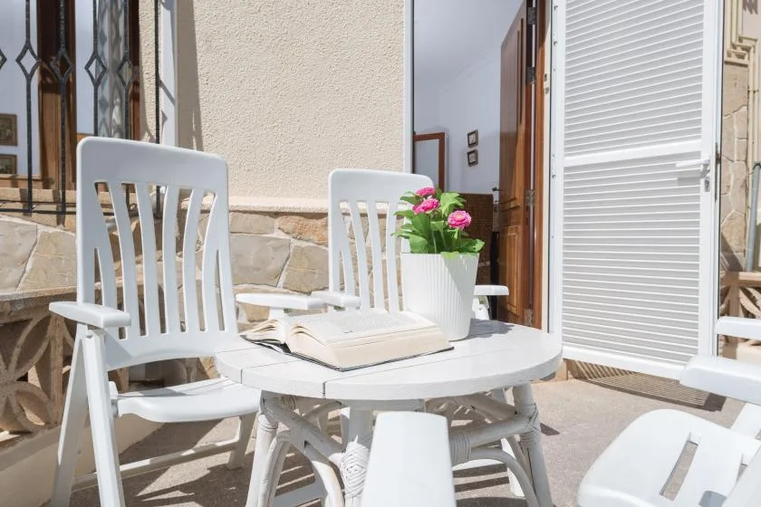A sunny outdoor patio with white seating, a table, and potted flowers.