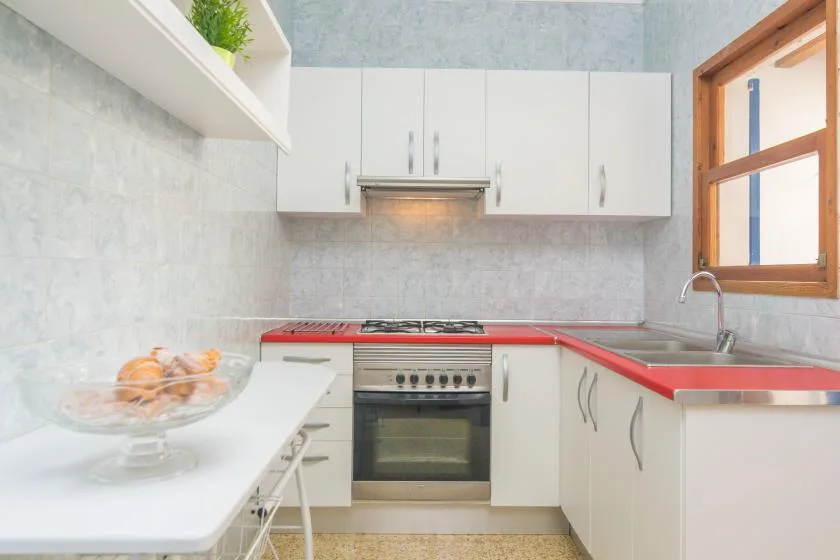 A bright kitchen with white cabinets, red countertops, and a built-in oven.