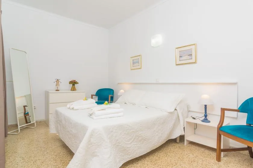A bright bedroom with a white bed, bedside tables, and turquoise seating.