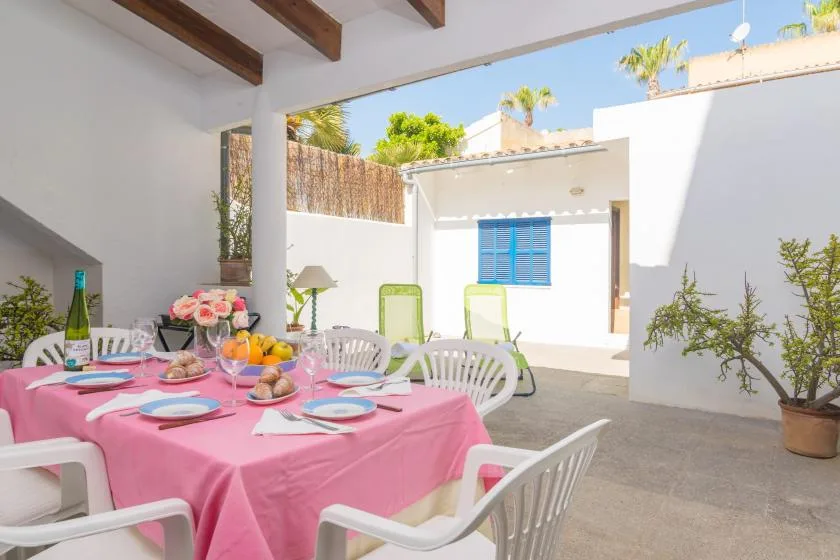 An outdoor dining area has a pink tablecloth and white chairs.