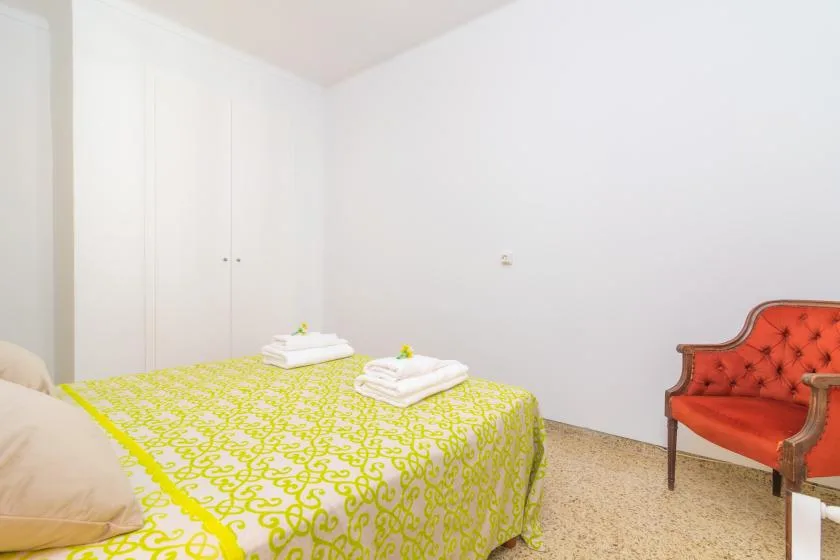 A bedroom with a bed covered in a bright patterned bedspread and a red armchair.