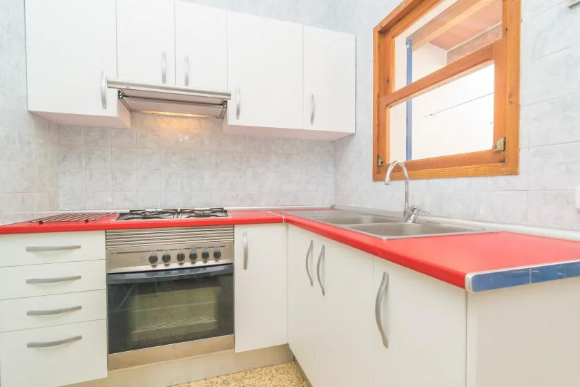 A bright kitchen with white cabinets, a red countertop, and a window above the sink.