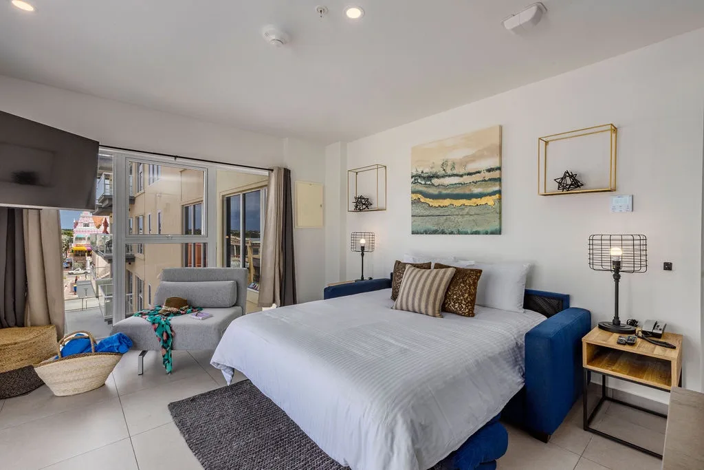 Unwind in your bright bedroom with coastal artwork, plush bedding, and a cozy lounge chair perfect for morning coffee or evening relaxation.