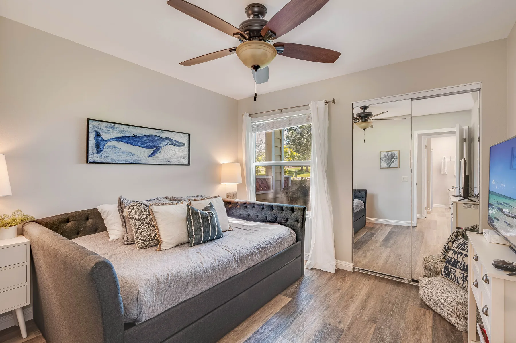 A bedroom with a bed, ceiling fan, and mirrored closet doors.